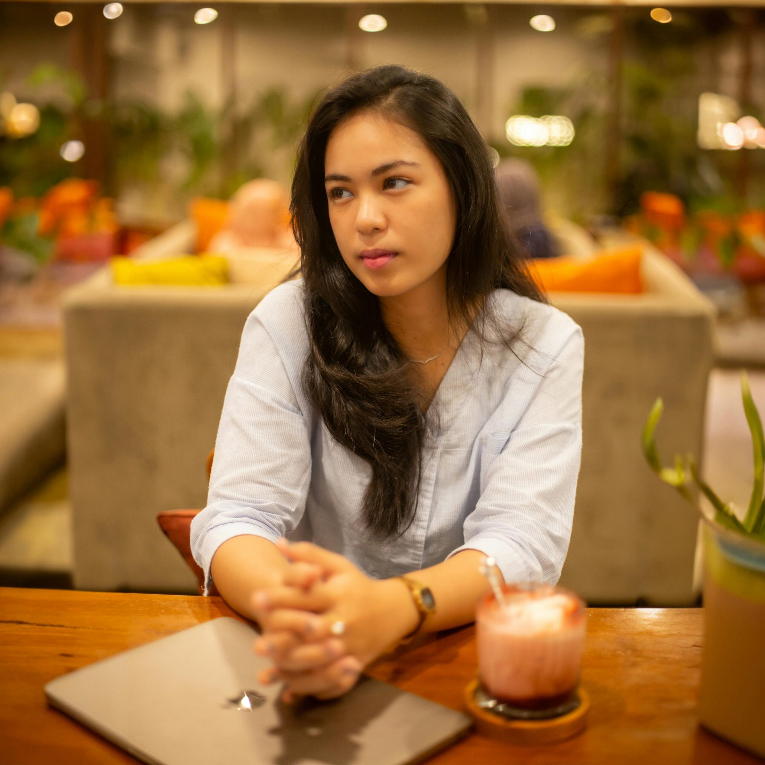 A young woman in a modern cafe with a relaxed mood, enjoying a warm ambiance in Pontianak, Indonesia.