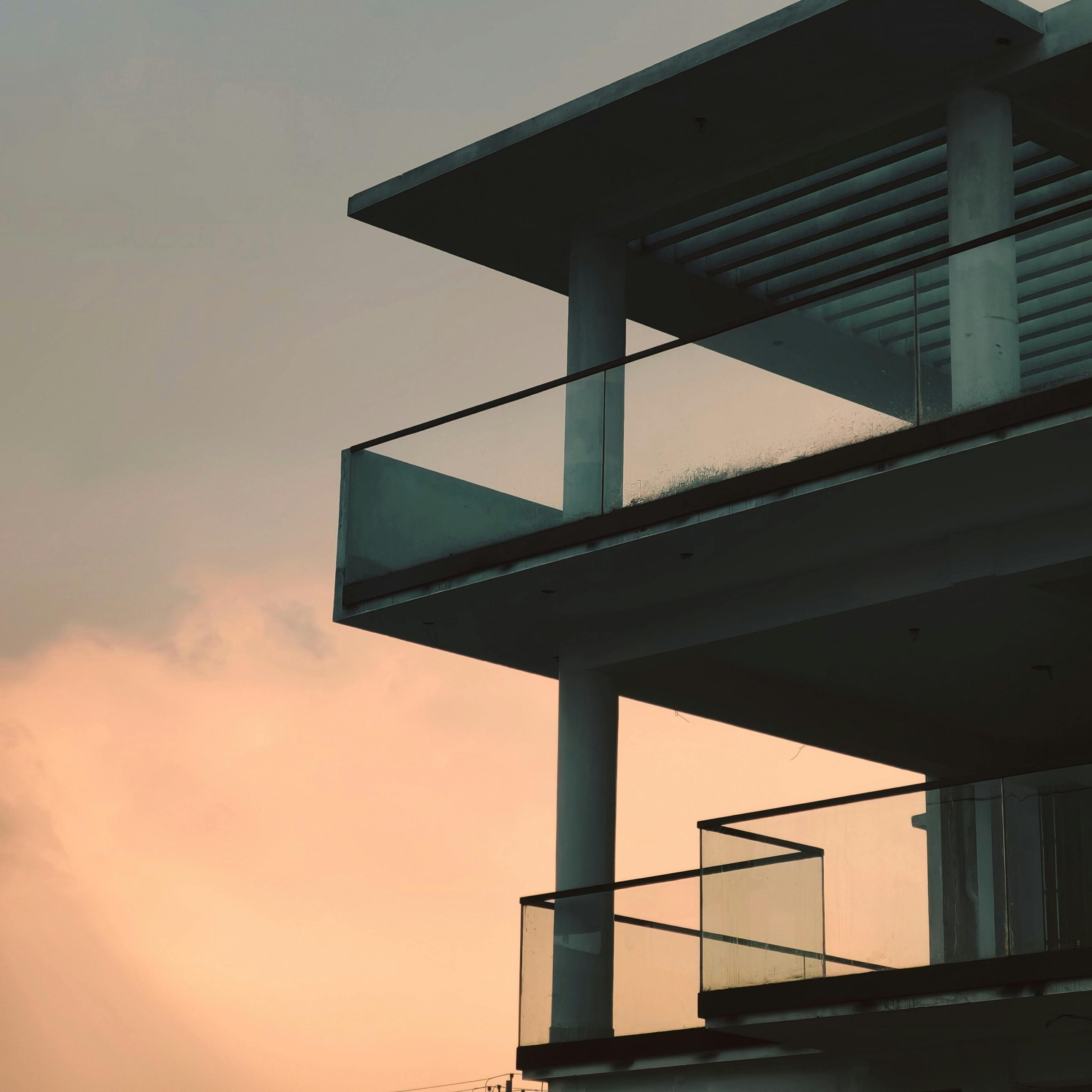 A sleek modern building with glass balconies silhouetted against a serene sunset sky.