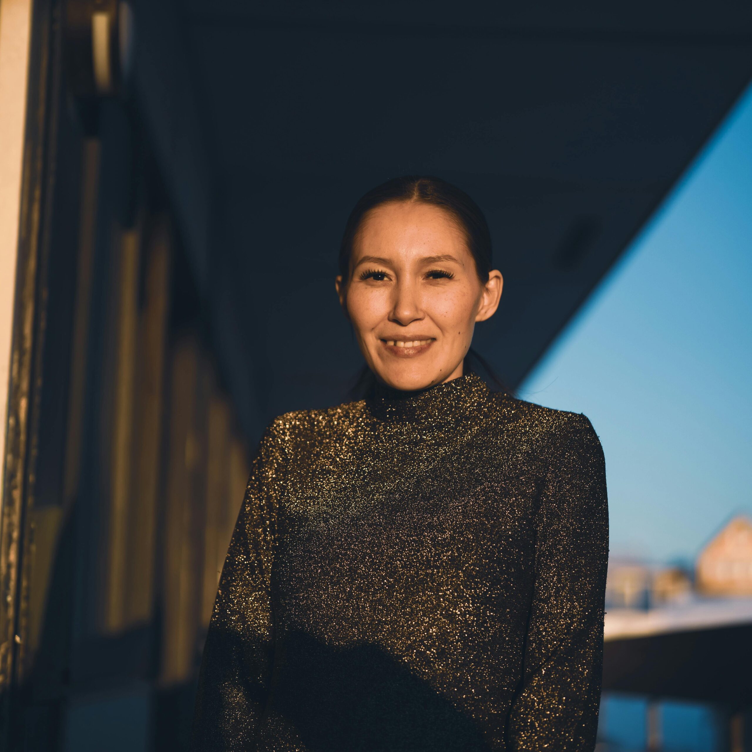 A woman smiles warmly in a glittery top during sunset in Nuuk, Greenland.