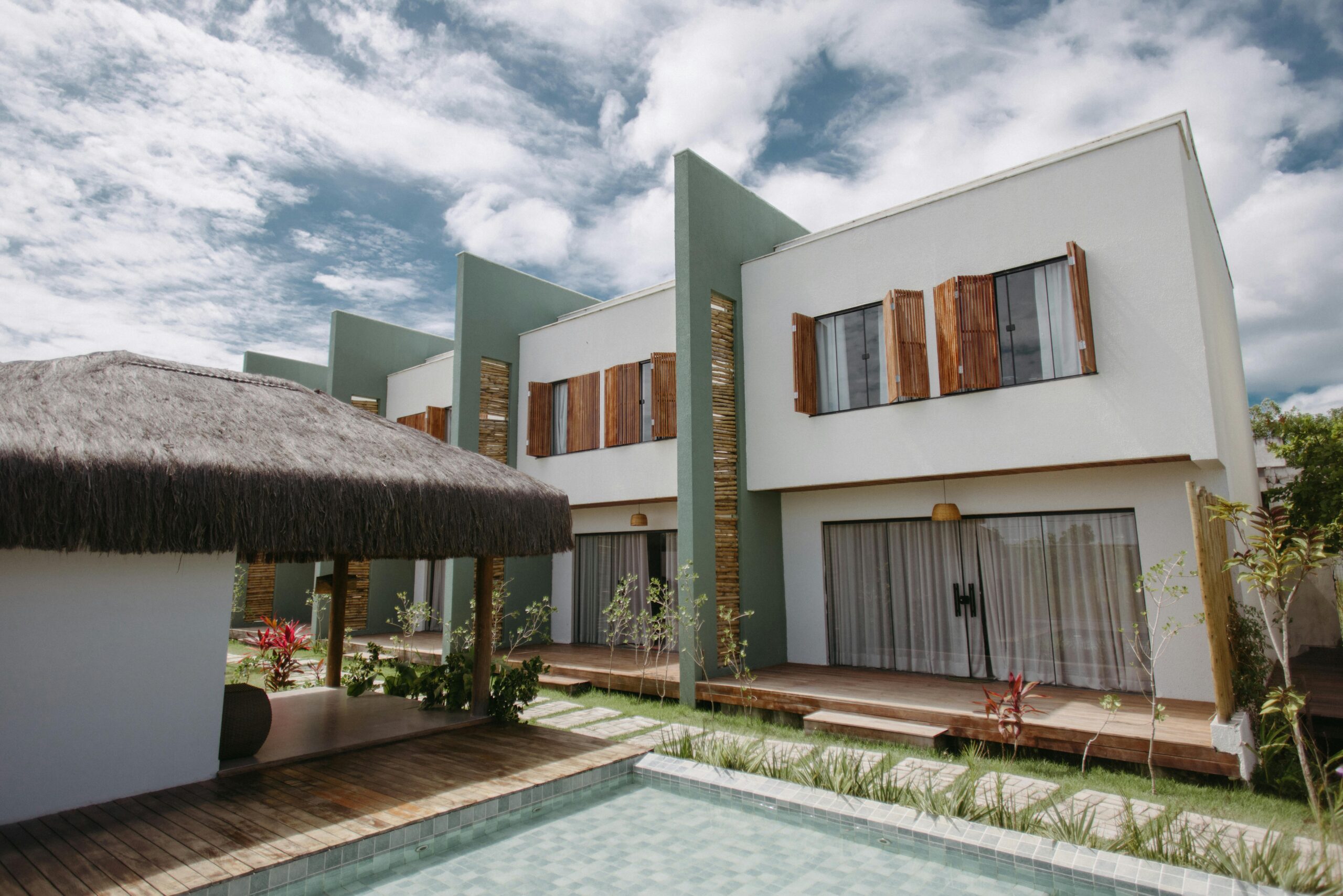 Stylish modern villas with wooden accents and thatched roofing by a pool under a vibrant sky in Bahia, Brazil.