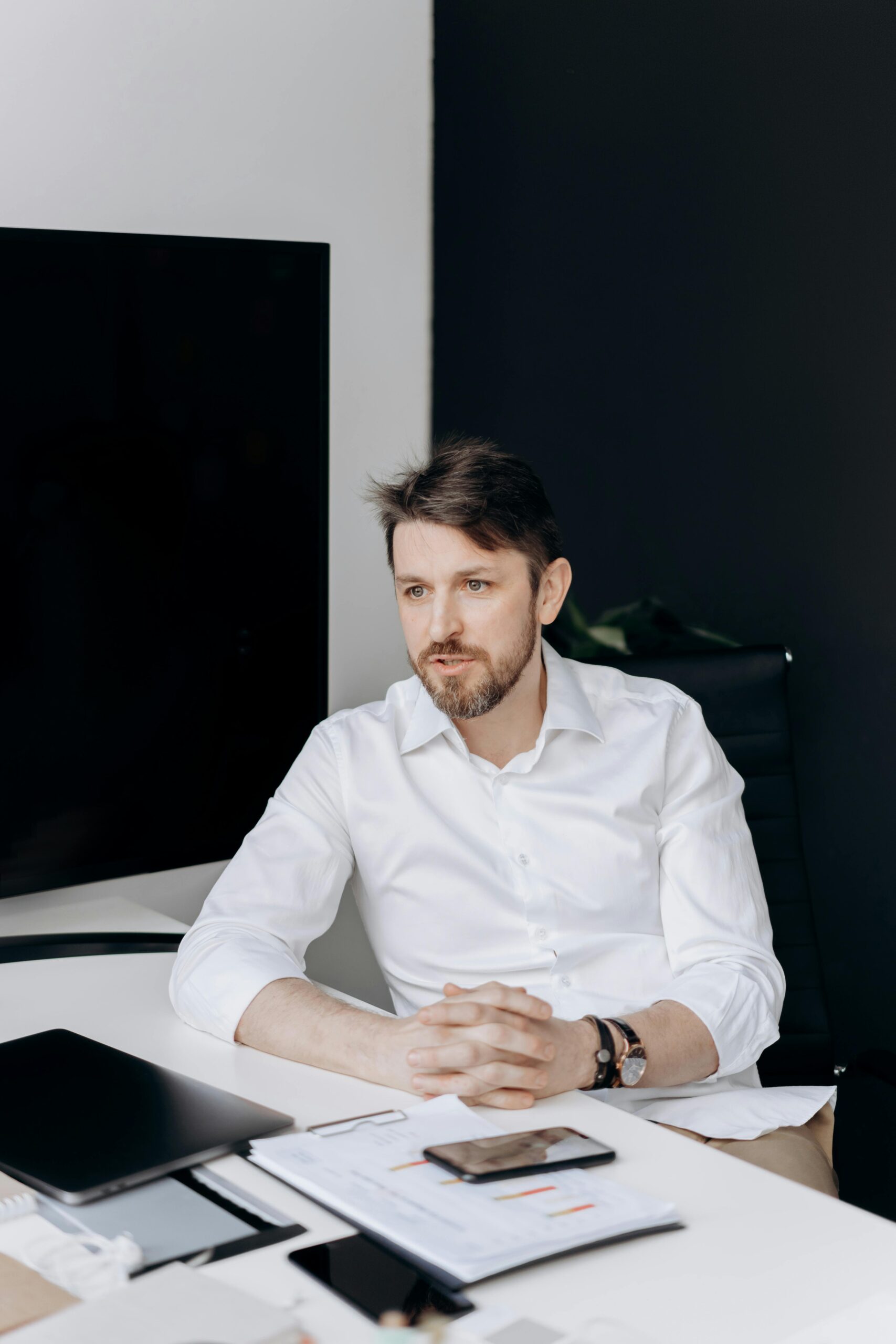 About Us Caucasian man with facial hair in a modern office, wearing a white shirt, deeply focused at his desk.