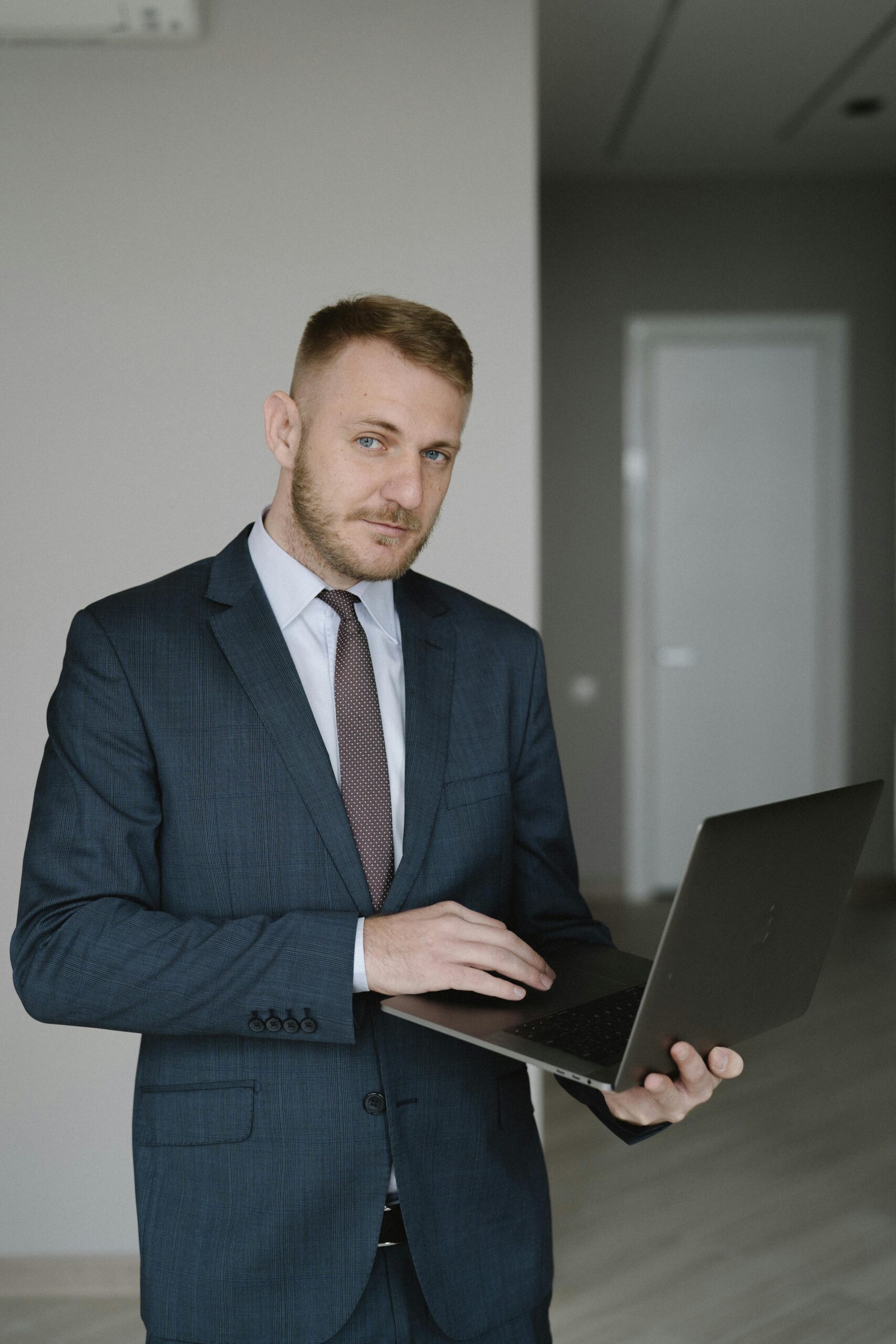 About Us Young businessman in a suit using a laptop indoors, embodying corporate professionalism.