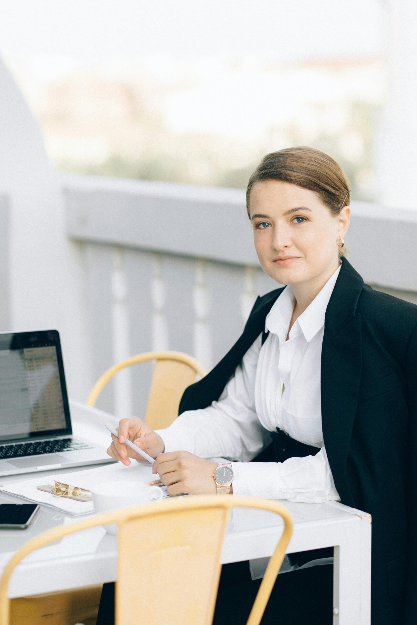 About Us Young woman in a black blazer, working outdoors on a laptop, embodying professionalism.